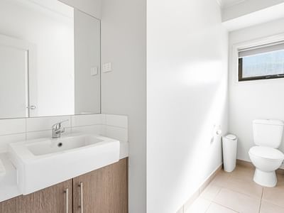Clean and modern bathroom with white sink, mirror, toilet, and tiled floors.