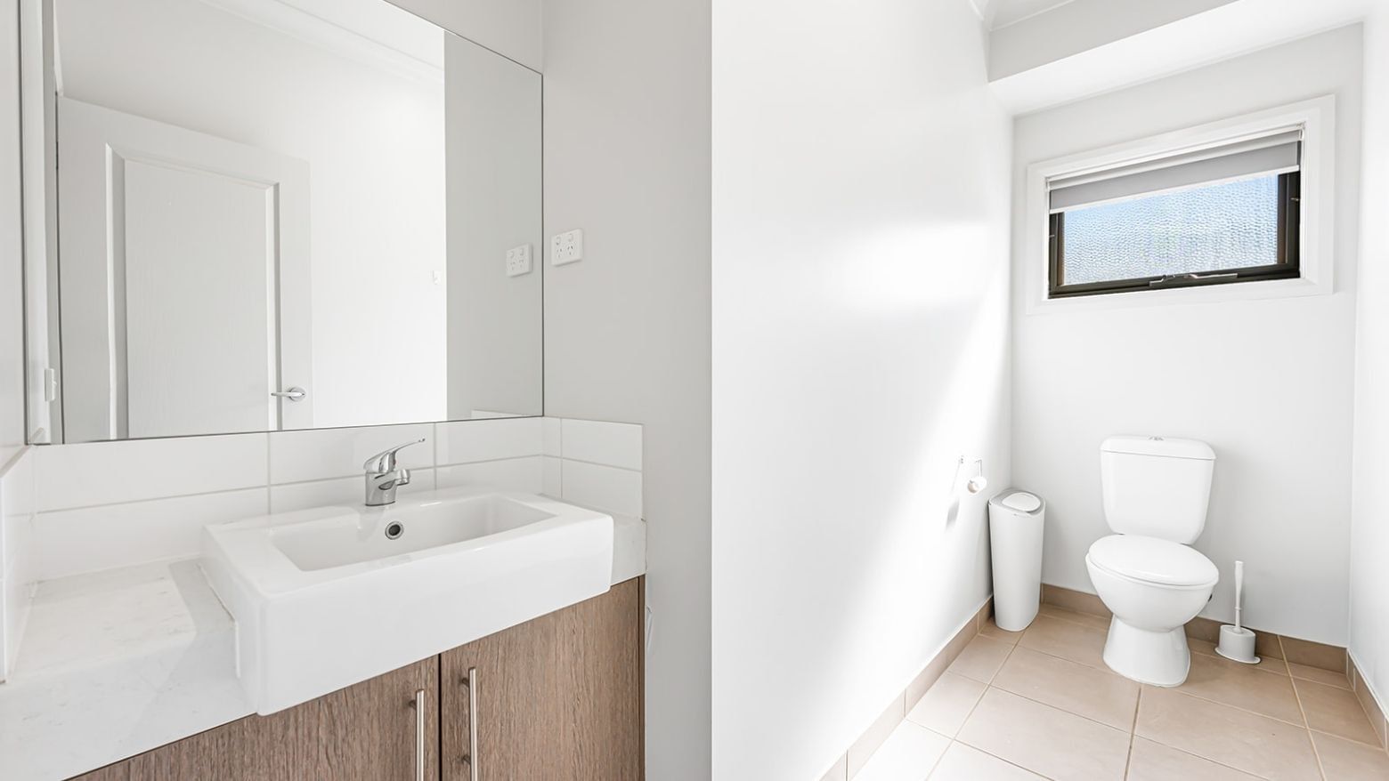 Clean and modern bathroom with white sink, mirror, toilet, and tiled floors.