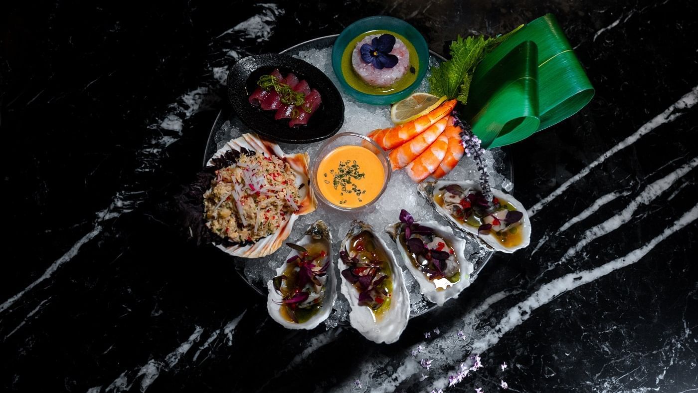 A platter of oysters, vegetables, and sauces on a marbled table in May Fair Kitchen at The May Fair Hotel