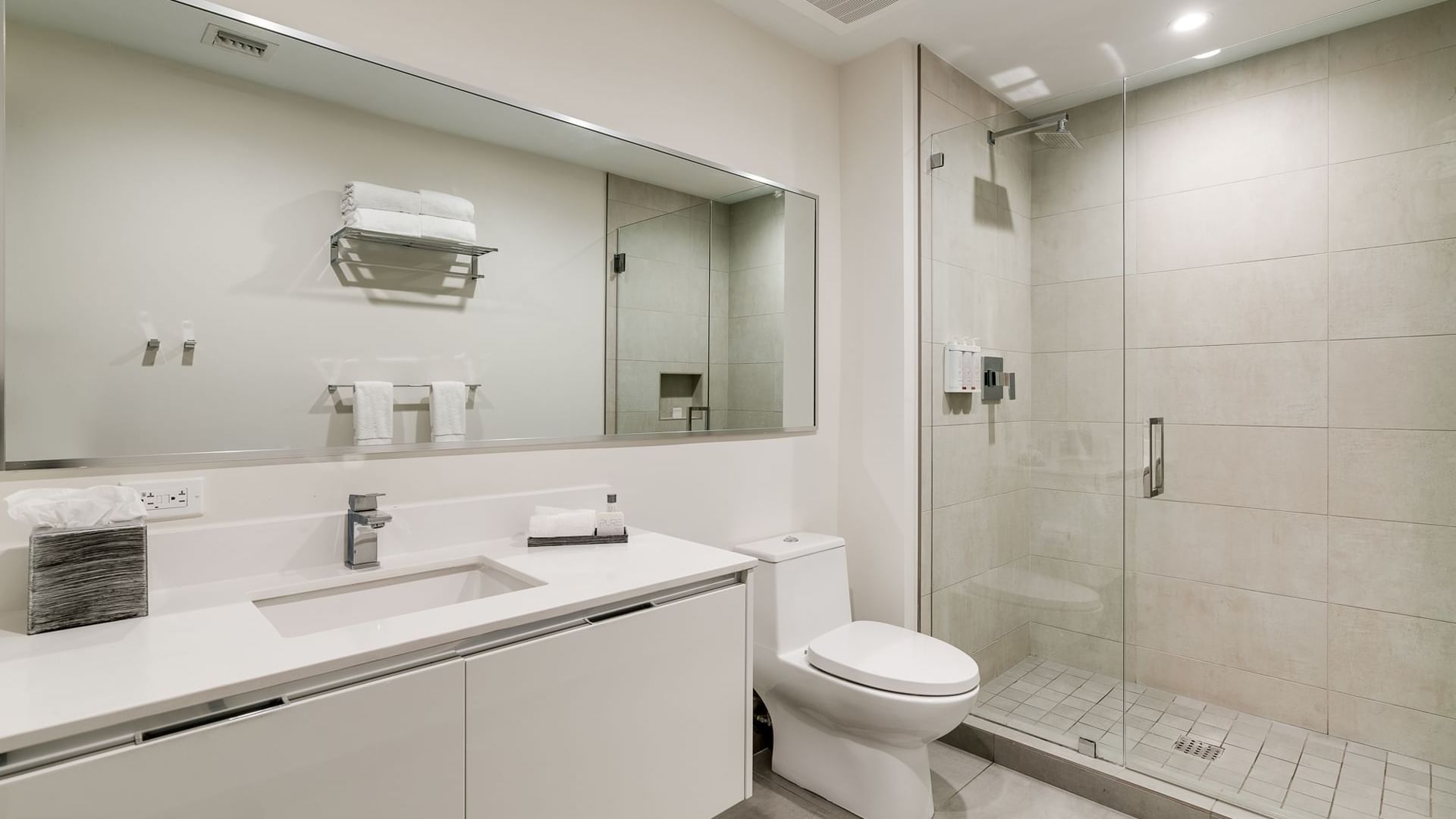 A modern, clean bathroom with a large mirror, glass shower door, and white fixtures.