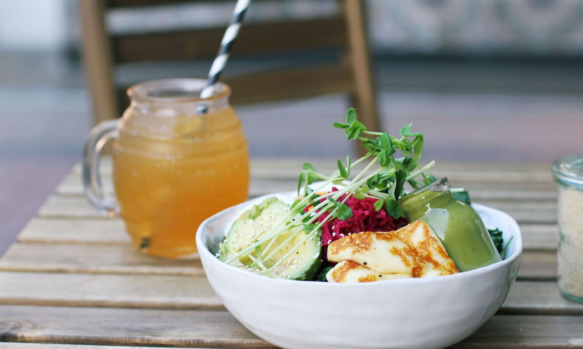 Girdlers Café healthy bowl at Elysium Hotels with avocado and halloumi cheese is beside an iced tea glass on a wooden table