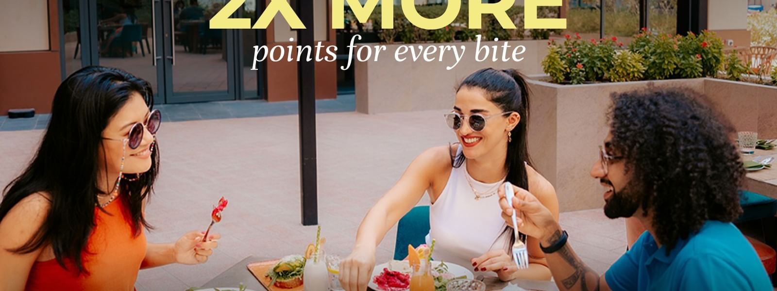 Three friends enjoying a sunny outdoor meal together with colorful dishes and drinks on the table.