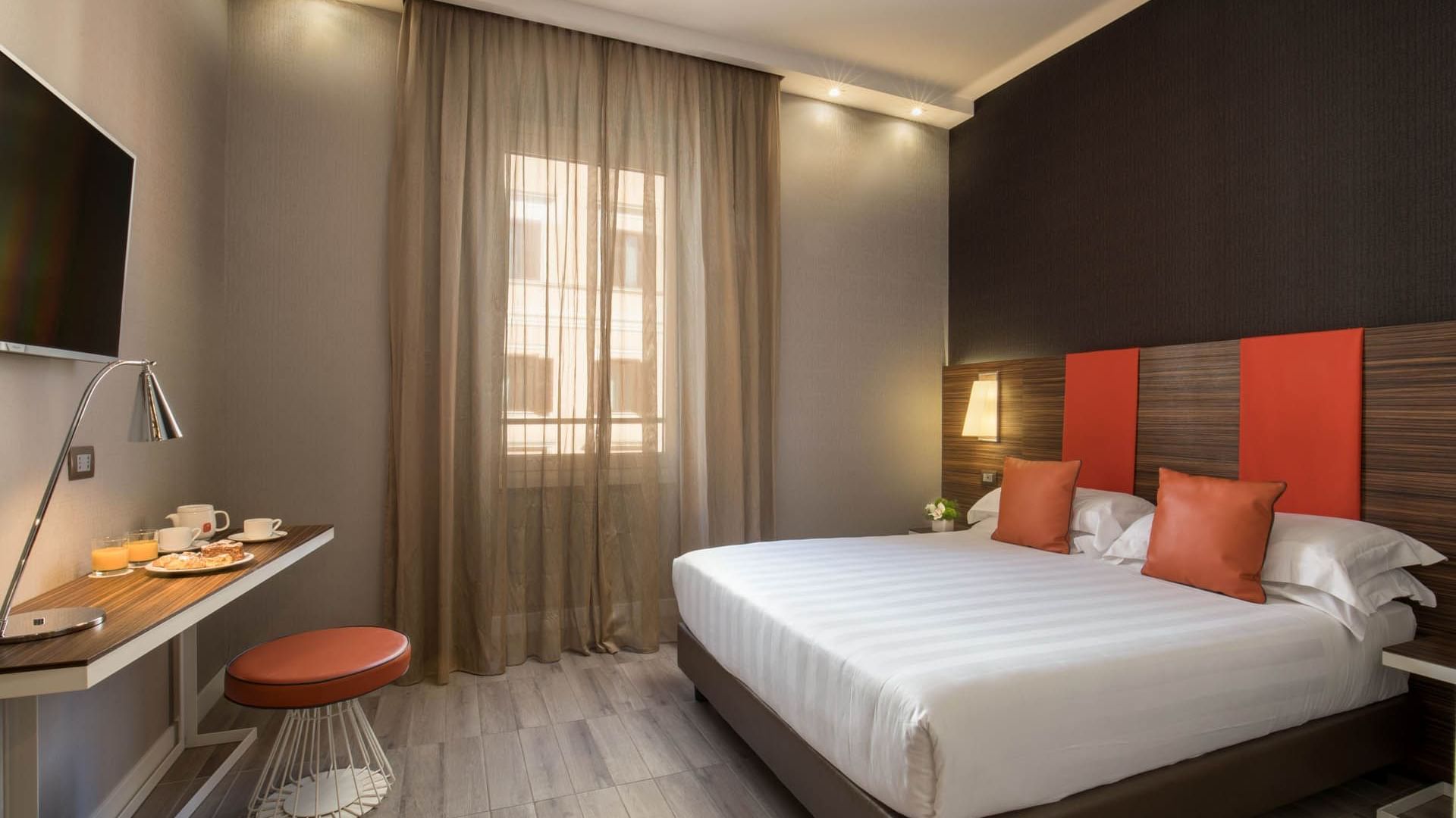 Smart room featuring a double bed with orange cushions, a dining table, and curtains letting in light at The Republic Hotel