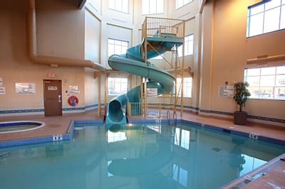 Spiral blue water slide by a hot tub, surrounded by an indoor pool with tiled deck at Glenmore Inn & Convention Centre