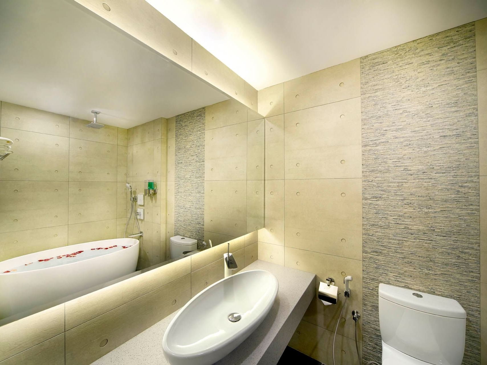 Image 75: Elegant bathroom with a bathtub filled with rose petals, a modern sink, and stone-patterned walls at Orchard Grand Court