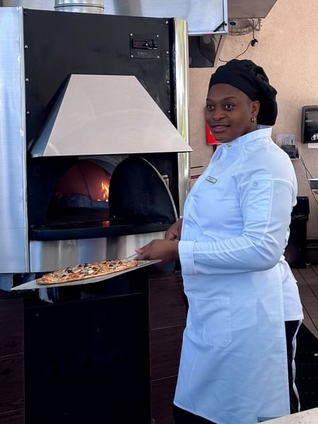 Chef in white attire by a fired oven holding pizza in Chickcharnie's Pizzeria & Grille at Warwick Paradise Island Bahamas