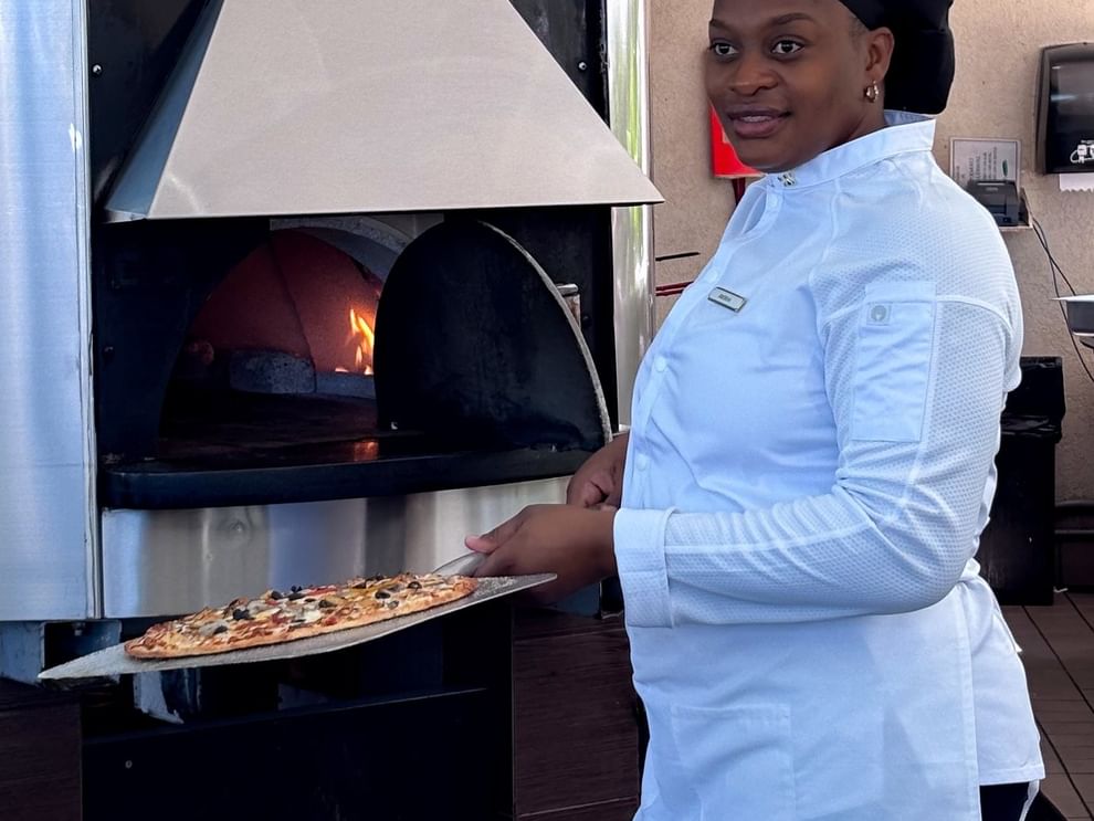 Chef in white attire by a fired oven holding pizza in Chickcharnie's Pizzeria & Grille at Warwick Paradise Island Bahamas