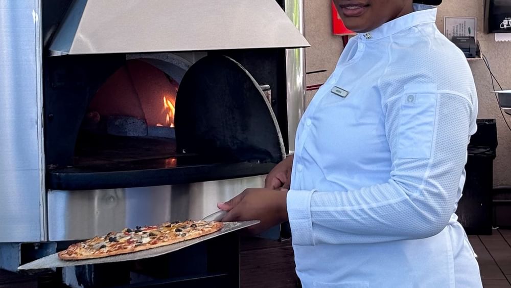 Chef in white attire by a fired oven holding pizza in Chickcharnie's Pizzeria & Grille at Warwick Paradise Island Bahamas
