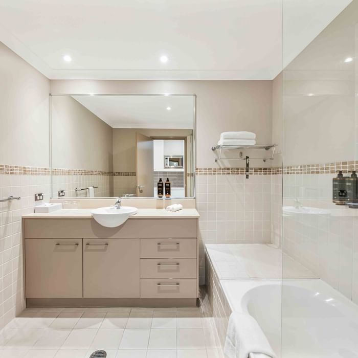 Bathroom with vanity, mirror, and bathtub, accented with tan tiles in One Bedroom Apartment at Mercure Kooindah Waters