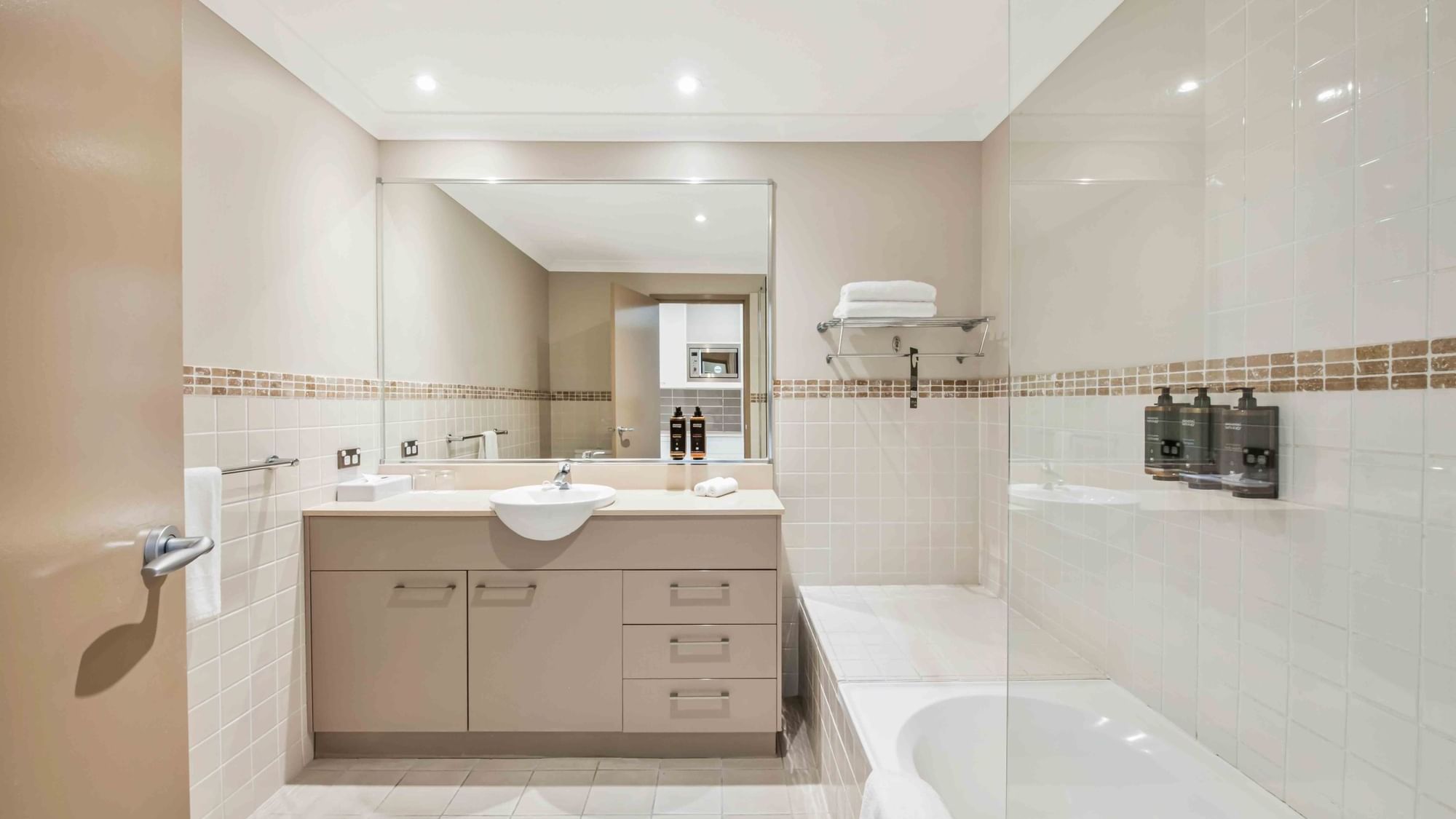 Bathroom with vanity, mirror, and bathtub, accented with tan tiles in One Bedroom Apartment at Mercure Kooindah Waters