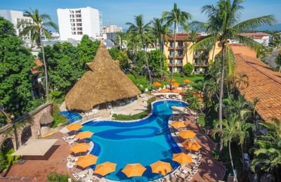 Resort with blue pool, thatched roof hut, lounge chairs, and palm trees in tropical setting.