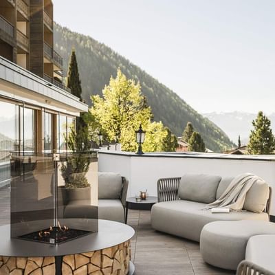 Outdoor lounge with fire pit, gray couches, and mountain view on a clear day.