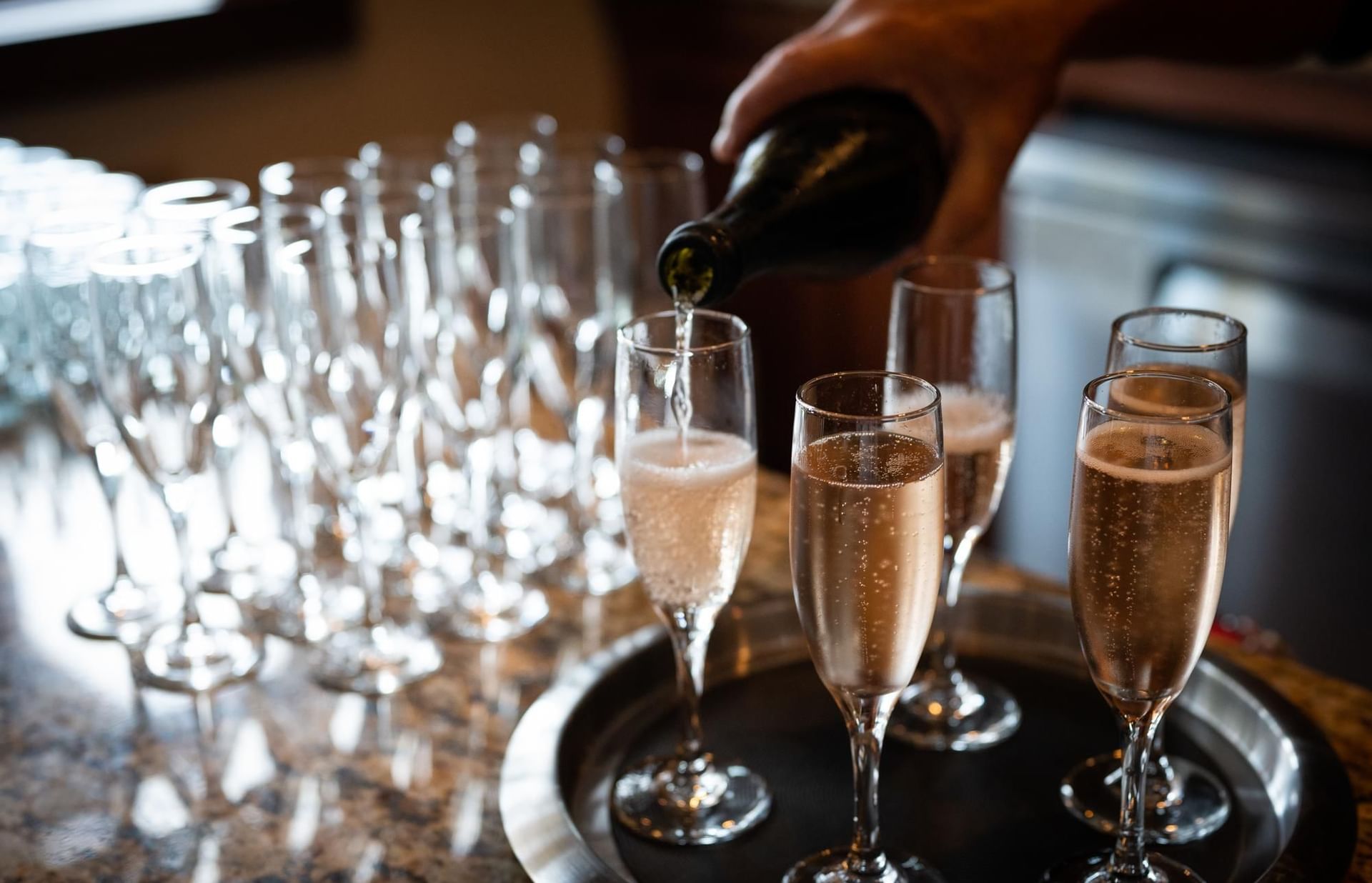 Champagne being poured into a wine flute accompanying other glasses on a serving tray