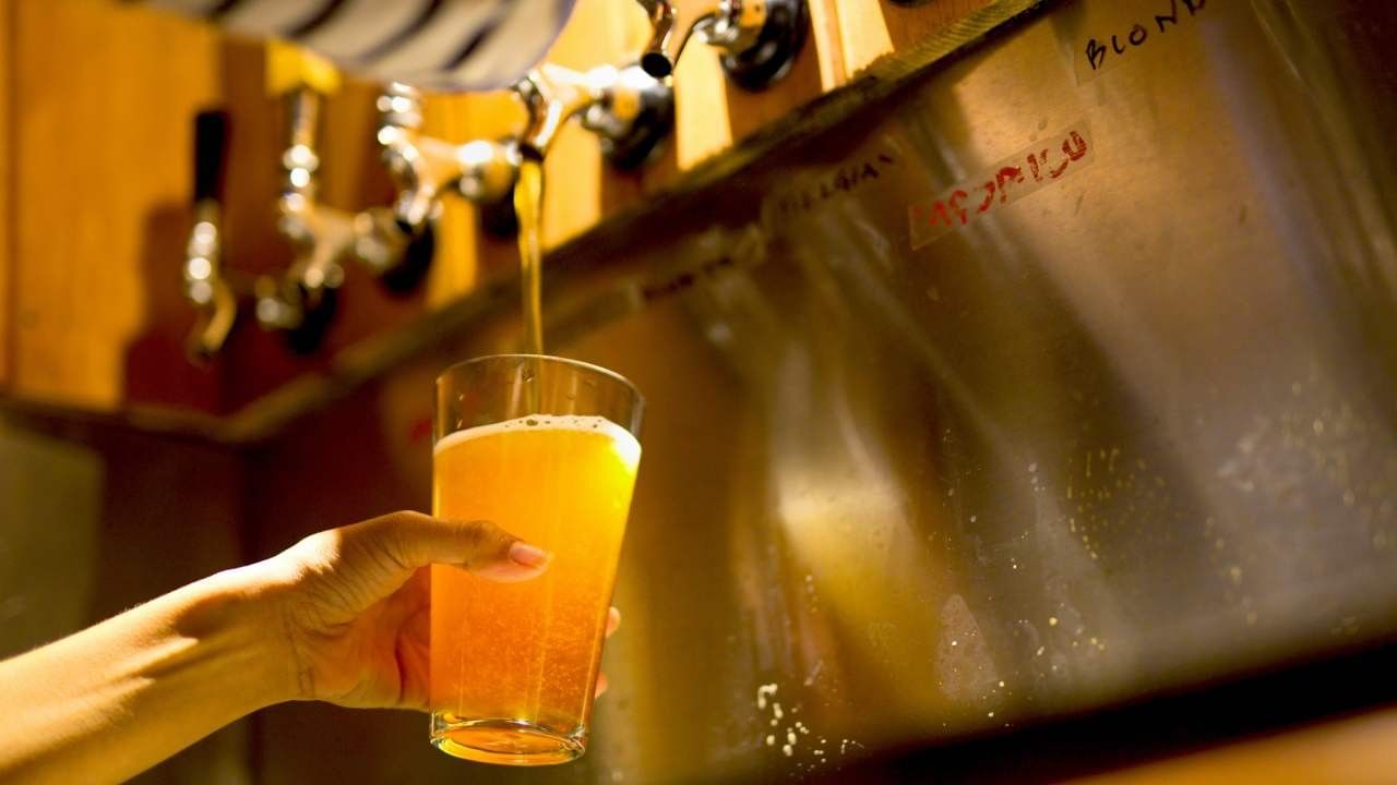 Close up of a person pouring a glass of amber beer from a stainless tap at Camino Real Pedregal Mexico