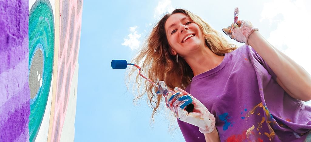 girl holding a paint roller next to street art