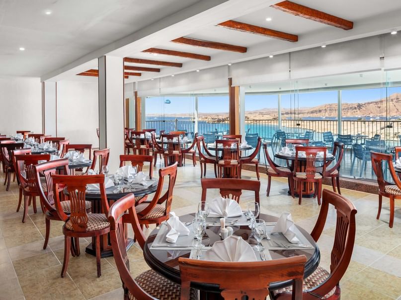 Empty dining room with tables and chairs, large windows, and a view of the ocean and mountains.