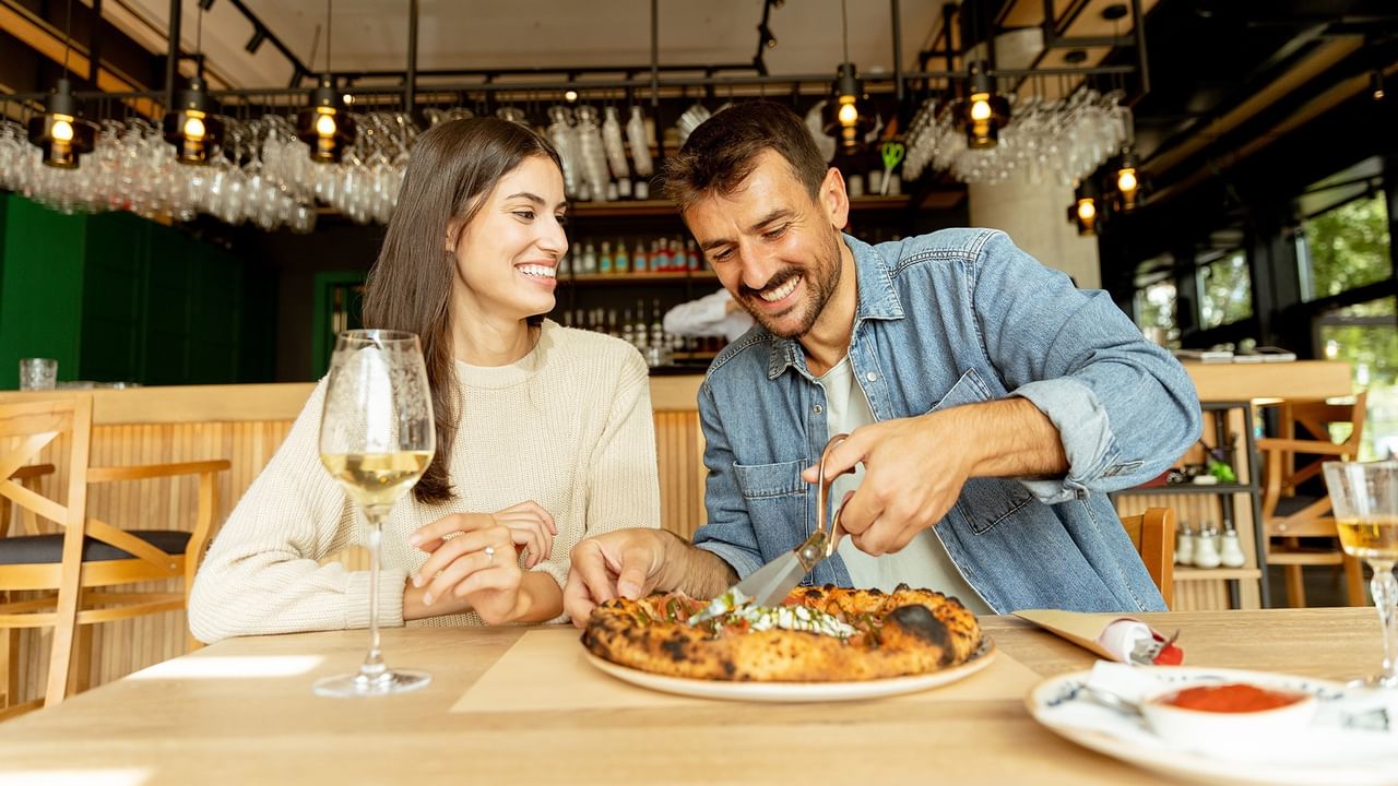 Couple dining together with a wine glass and pizza on a restaurant table for Picnic on Vancouver's North Shore.