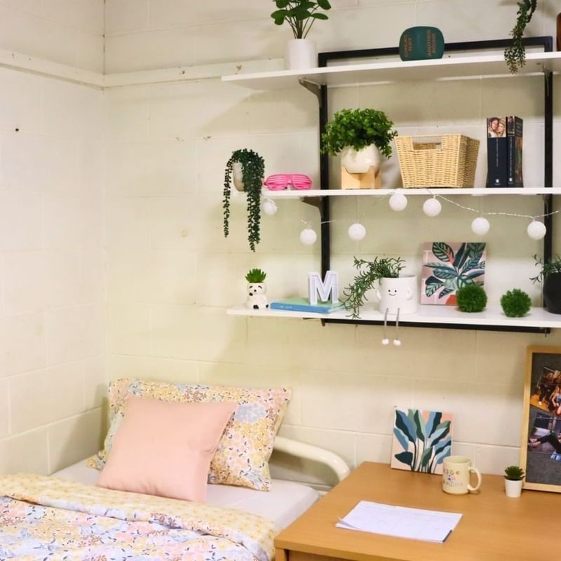 A cozy room with a bed, desk, and shelves with plants at La Trobe University - Units.