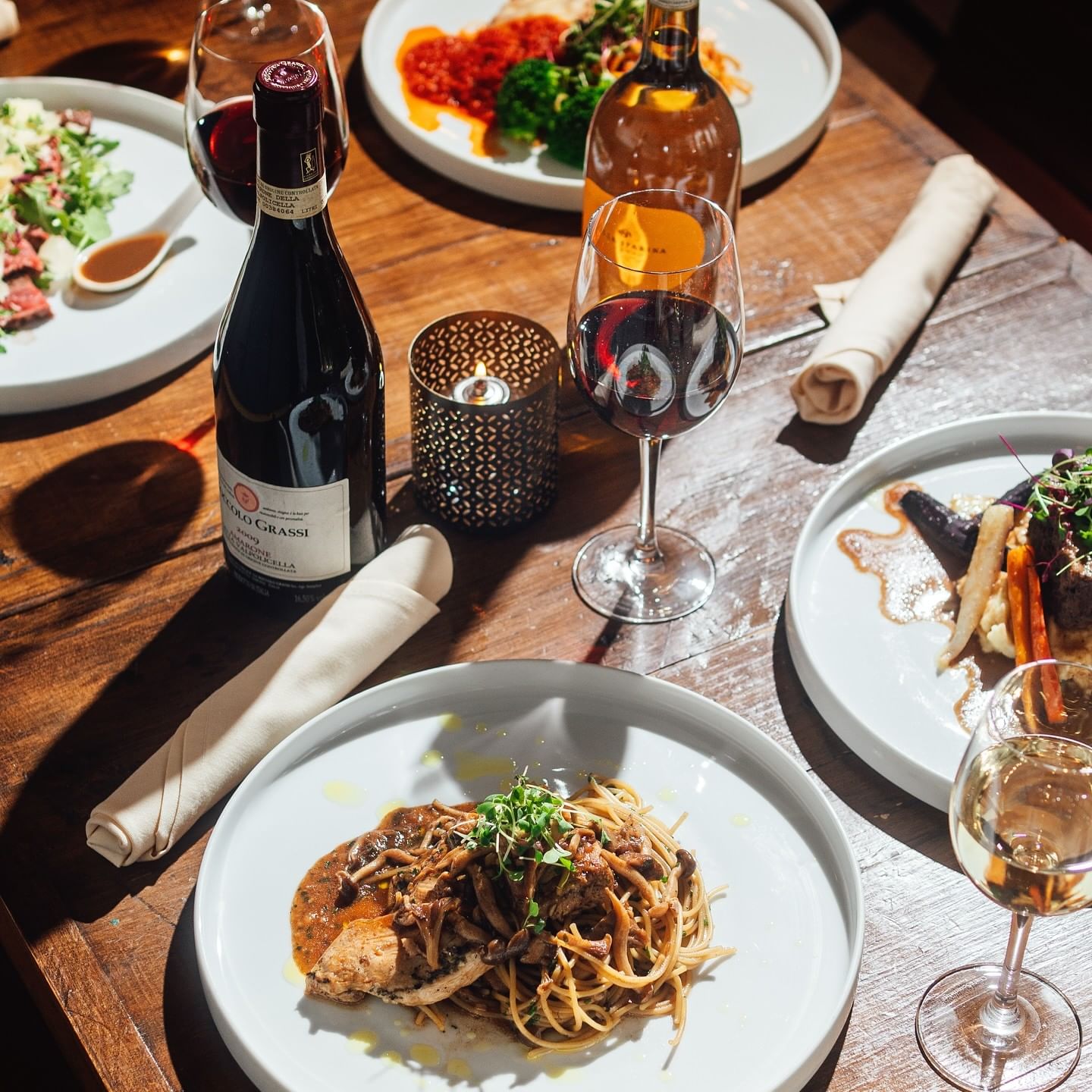 Italian dishes featuring savory mushroom pasta, wine bottles, and filled glasses on a candlelit table at Gattara