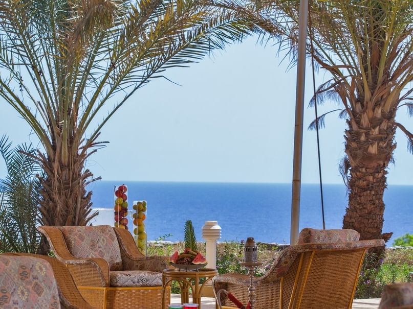 Outdoor lounge area with wicker furniture and ocean view under a beige canopy.