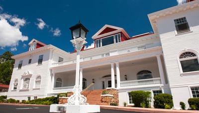 A beautiful bright sunny day showing the front exterior of the elegant white Stanley Hotel with red roofs