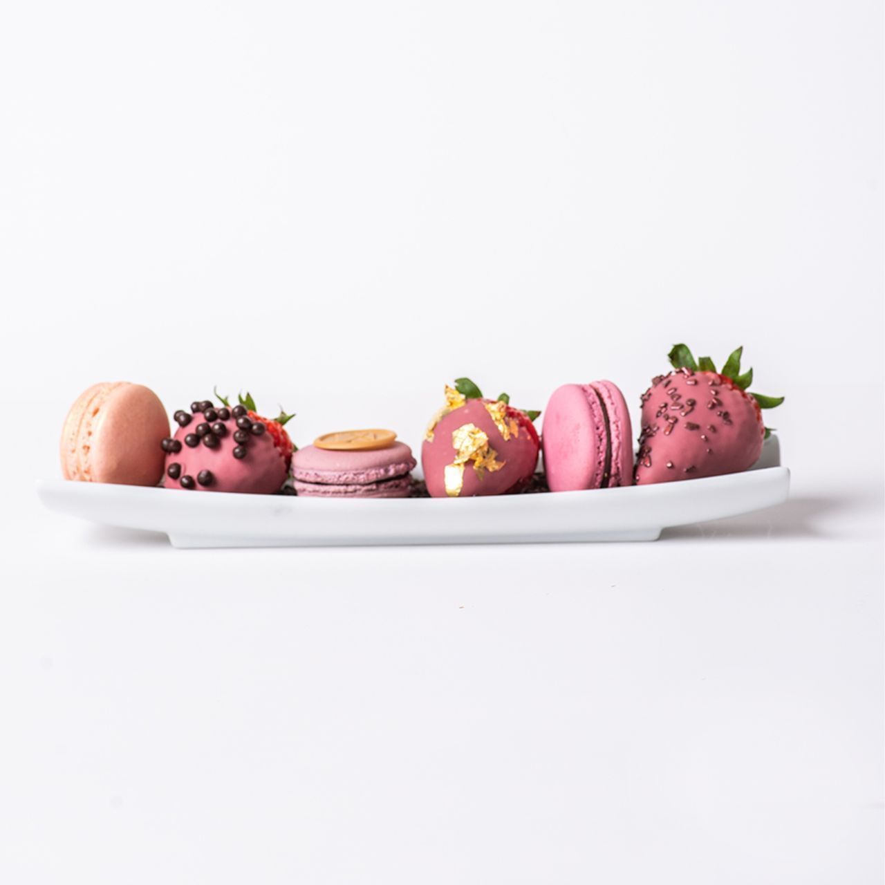 A white plate with an assortment of pink and gold macarons and chocolate-covered strawberries.