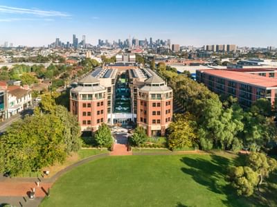 Aerial view of Amora Herencia Riverwalk Melbourne with tree-lined streets, and a vast city skyline in the distance