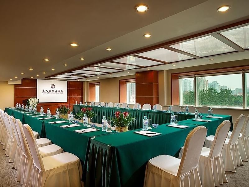 U-shaped table set up facing the projector screen by the window in Meeting Room 3 at Celebrity International Grand Hotel 