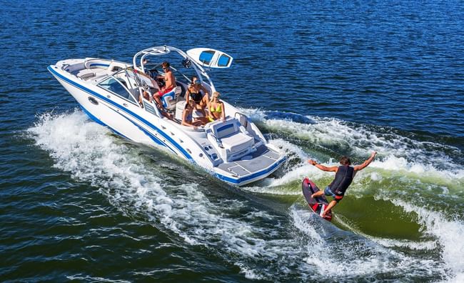 A man wakeboarding on a lake behind a white motorboat filled with several passengers at Shangri-La Resort and Golf Club