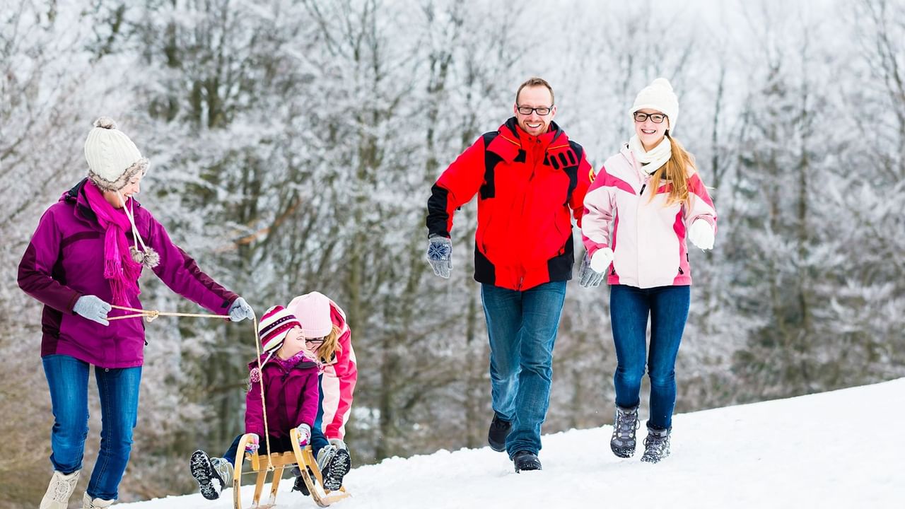 couple walking in the snow and mom pulling children on a sled