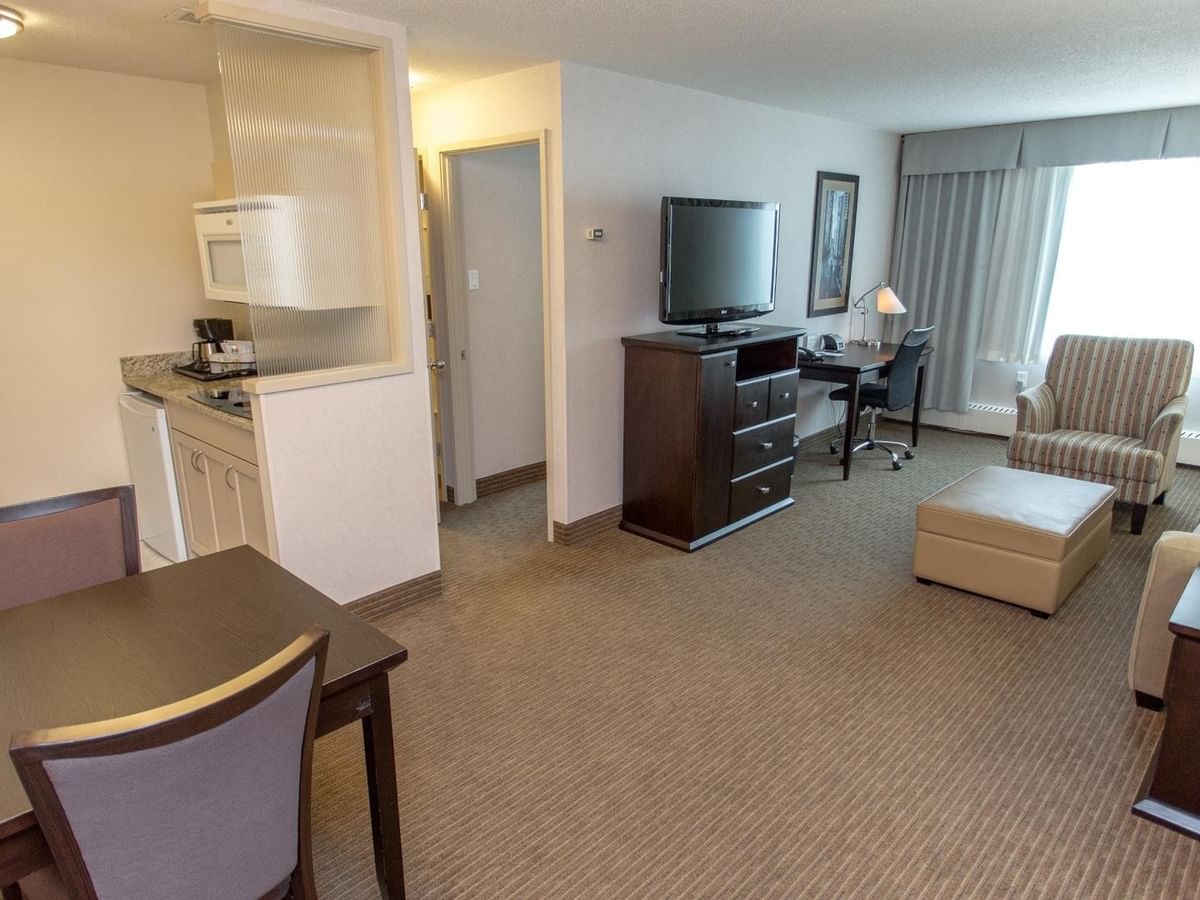 Hotel suite with dining area, kitchenette, sofa, TV and work desk.