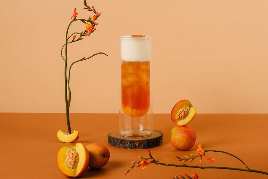 Tall glass of iced tea topped with foam, surrounded by peach slices and vibrant flowers in Park Lounge at Park Hyatt Saigon