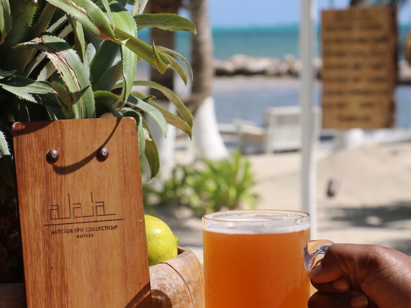 A person holding a beer in front of a wooden sign at Alaia Belize Autograph Collection