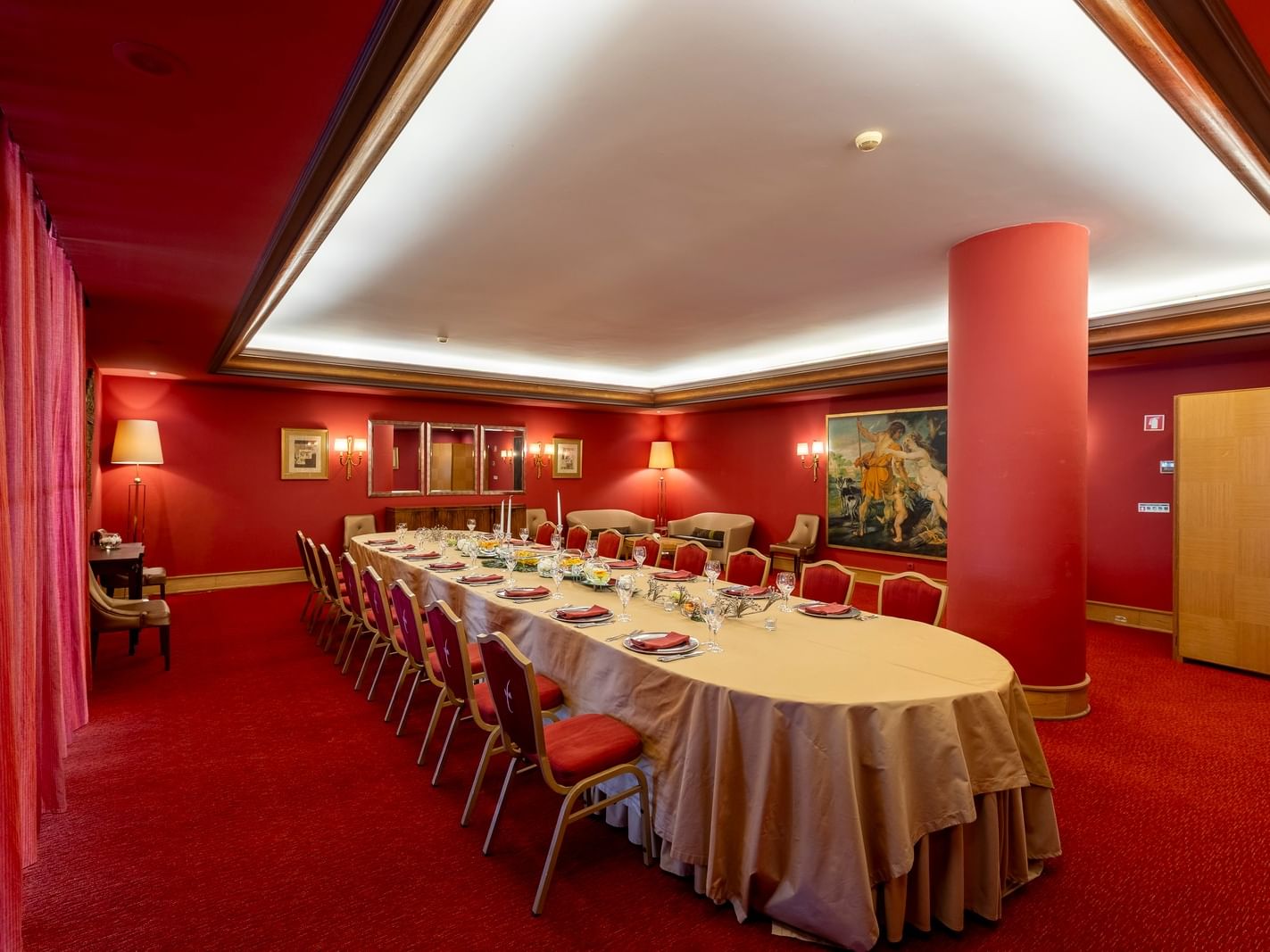 Sala con mesa larga, sillas rojas, paredes rojas, cortinas rojas y pintura en la pared.