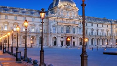 The Louvre Palace by glowing street lamps under a dark blue evening near Warwick Paris Champs Elysées
