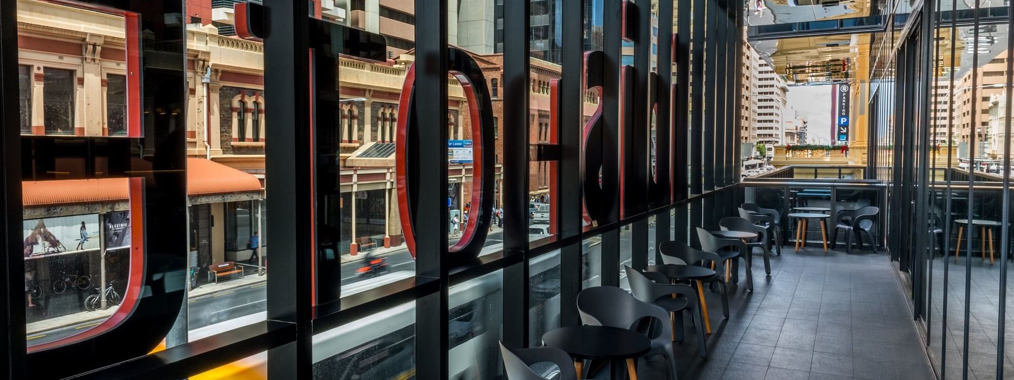 Modern balcony seating area with large windows offering city views at Ibis Adelaide