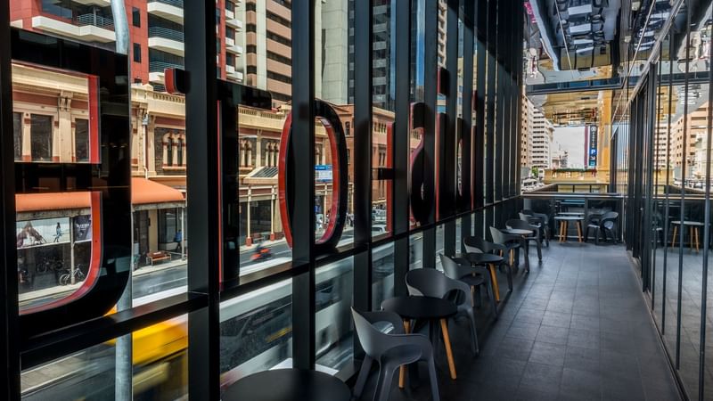Modern balcony seating area with large windows offering city views at Ibis Adelaide