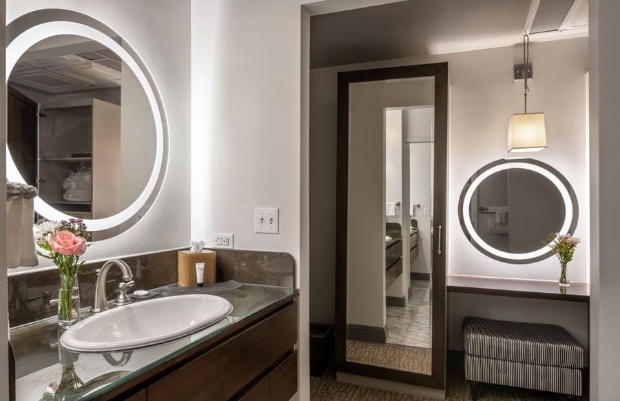Vanity with a round glowing mirror by a dark wood sink near a tall mirror in Grand Suite at Warwick San Francisco