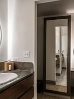 Vanity with a round glowing mirror by a dark wood sink near a tall mirror in Grand Suite at Warwick San Francisco