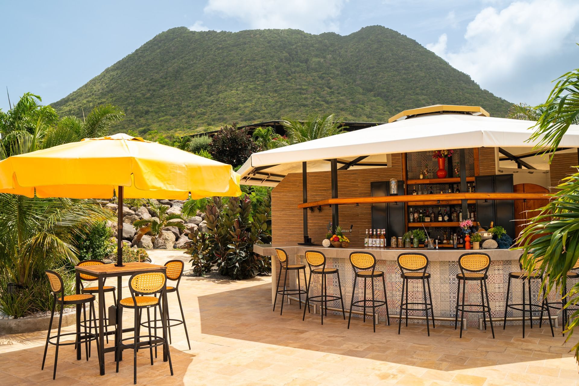 Buitenaanzicht van Pool Bar met gele parasols, omringd door weelderig groen en een berg bij Golden Rock Resort