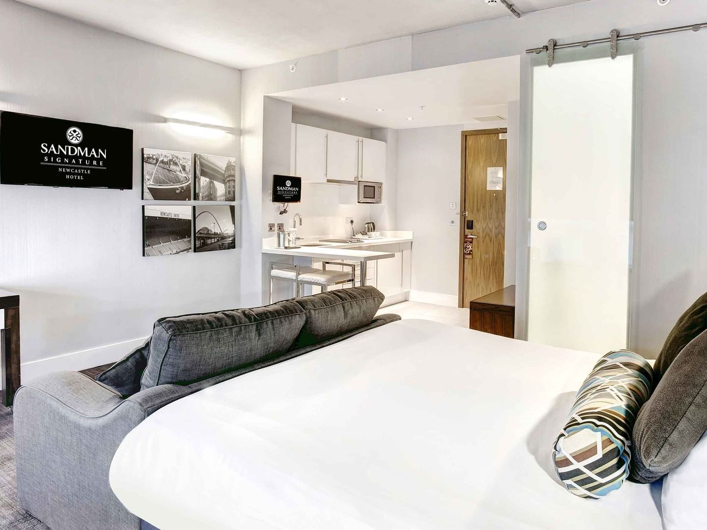The Corporate King Studio at Sandman Signature Newcastle Hotel with one super king ked (with premium pillow-top), one pull-out sofa bed, a flat-screen tv and small pantry with kitchen supplies and white pantry cupboards on the side