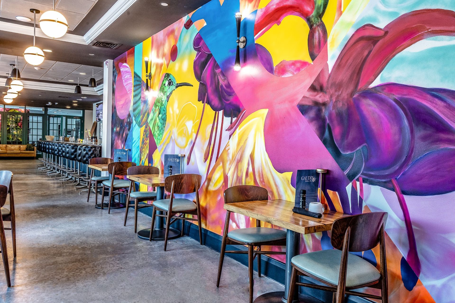 Bright mural of flowers with wooden tables and chairs at Gaudin Kitchen & Bar, The Barrymore Hotel