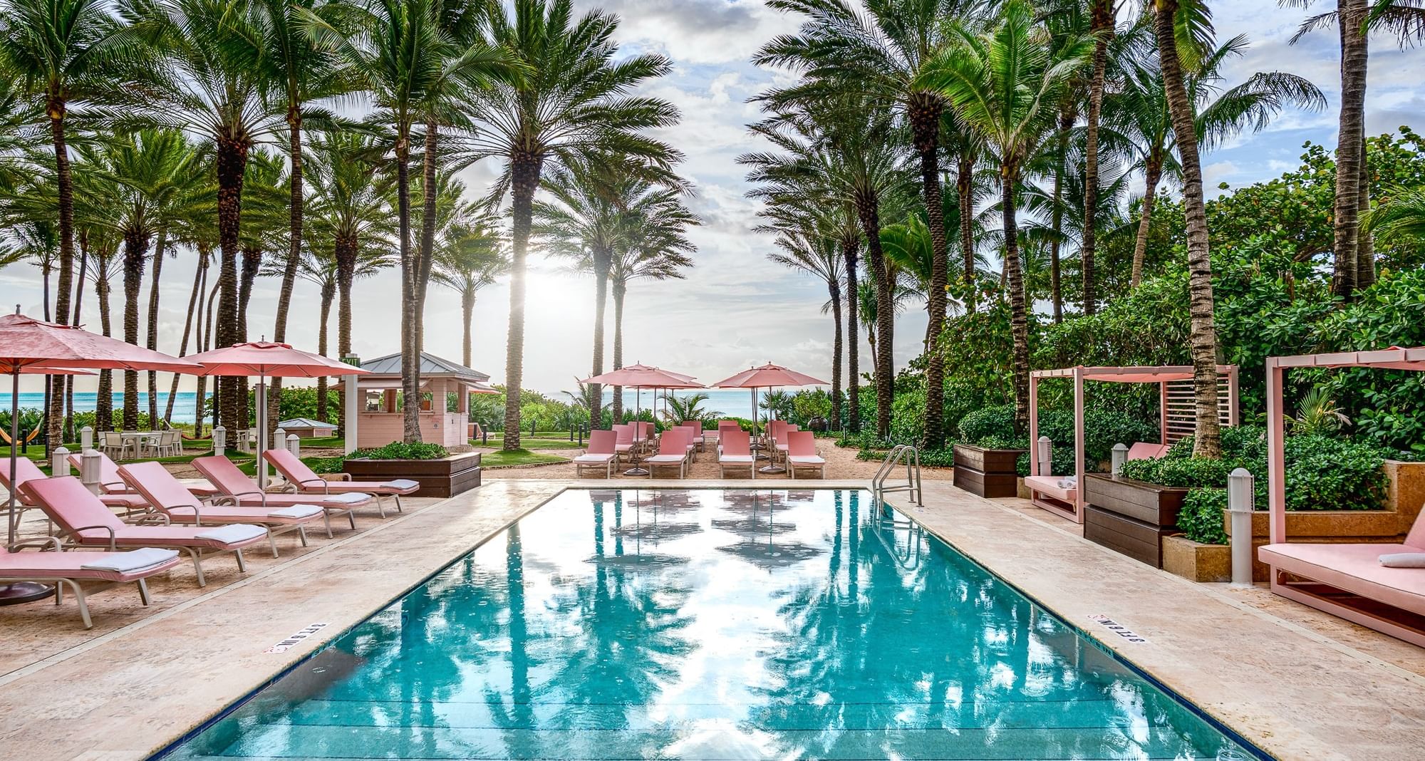 Outdoor rectangular pool reflecting palm trees beside pink sun loungers under bright skies at Grand Beach Hotel Surfside
