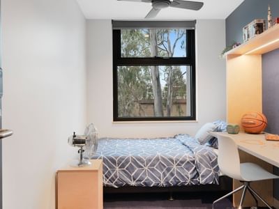 A cozy room with bed, desk, chair, and window at La Trobe University - North and South Apartments.