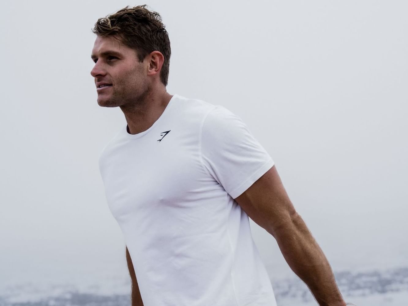 Homem a alongar os músculos das pernas num corrimão junto ao mar, para o evento «Sculpt & Strength».