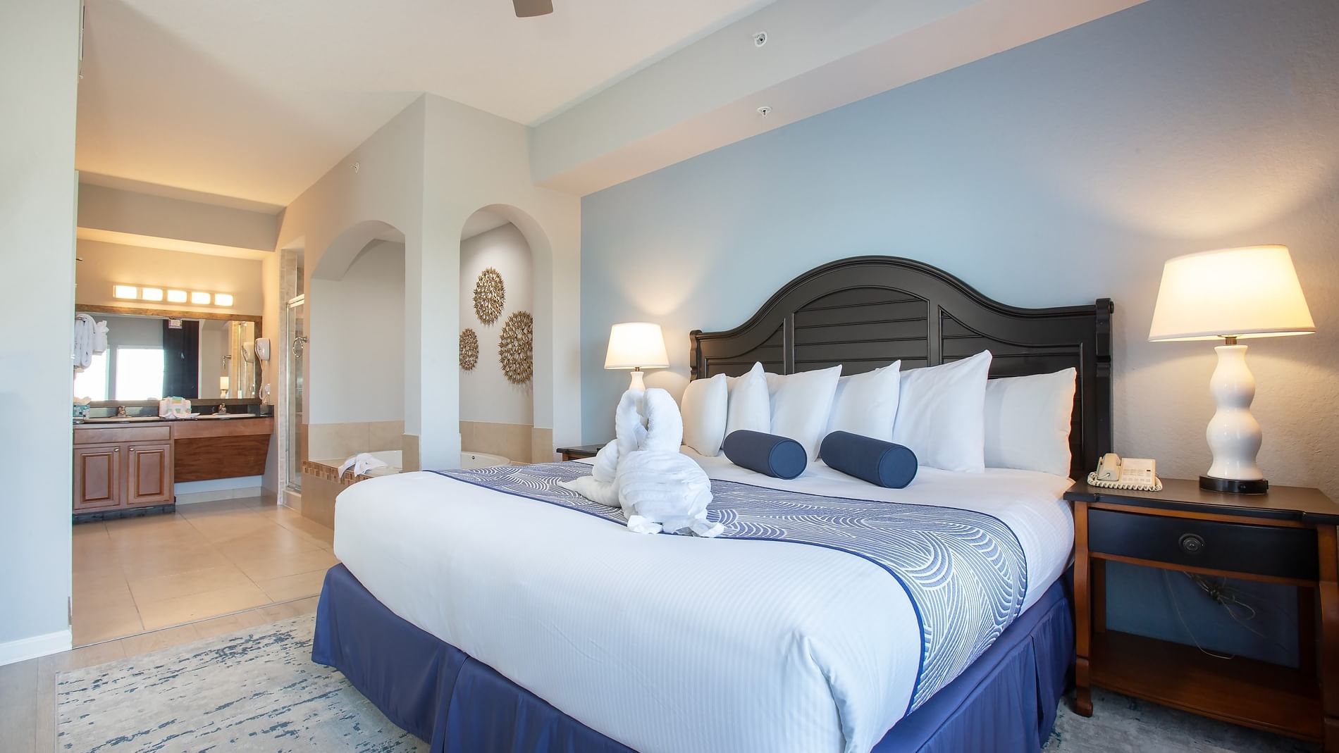 A wide view of a hotel room with a king-sized bed, nightstand, and lamp, with a bathroom in the background.