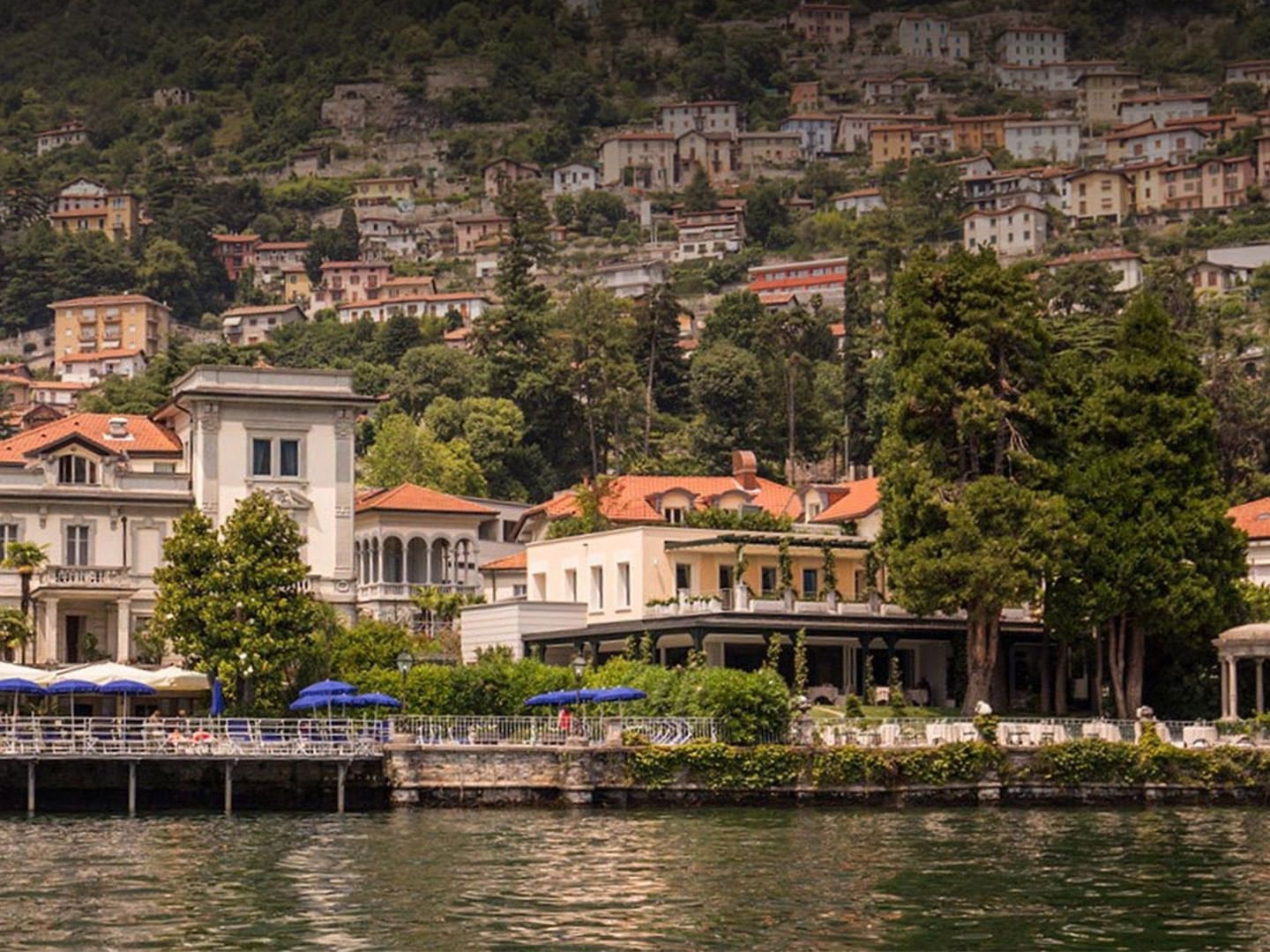 Scenic lakeside view of Lake Como with elegant villas and terraced homes nestled in lush hillside greenery near AG Hotels