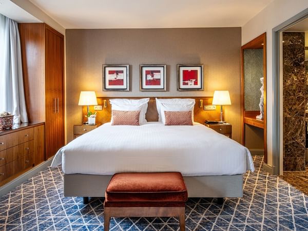 Elegant hotel room with large bed, wooden furniture, and artwork at Warwick Grand-Place Brussels.