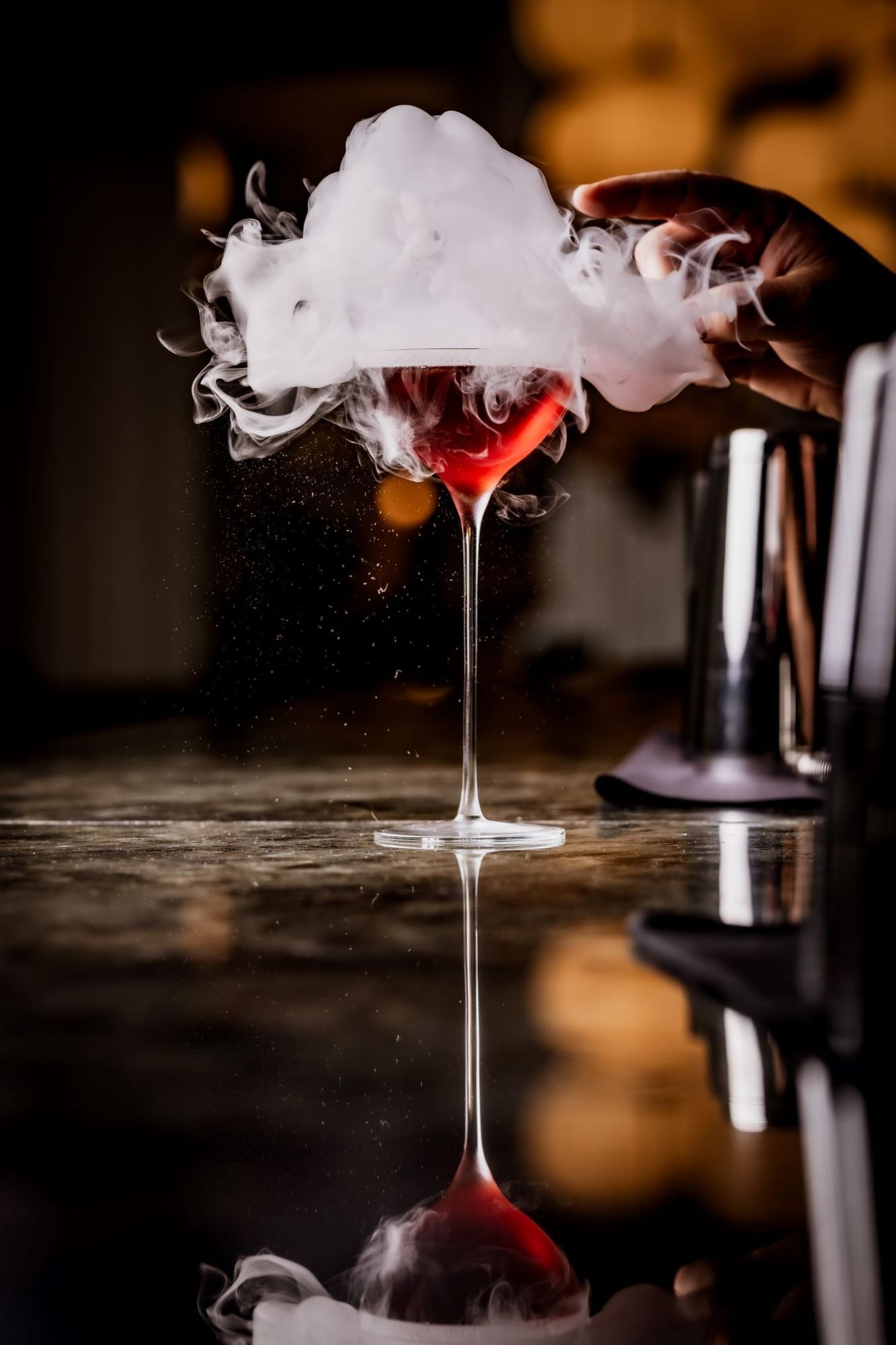 Hand popping the bubble to create a smoke effect to the Turkey, Sphere cocktail in a martini glass at The May Fair Bar