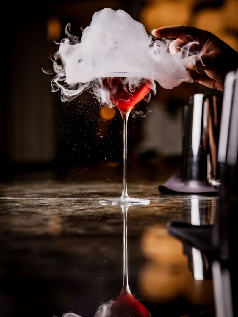 Hand popping the bubble to create a smoke effect to the Turkey, Sphere cocktail in a martini glass at The May Fair Bar
